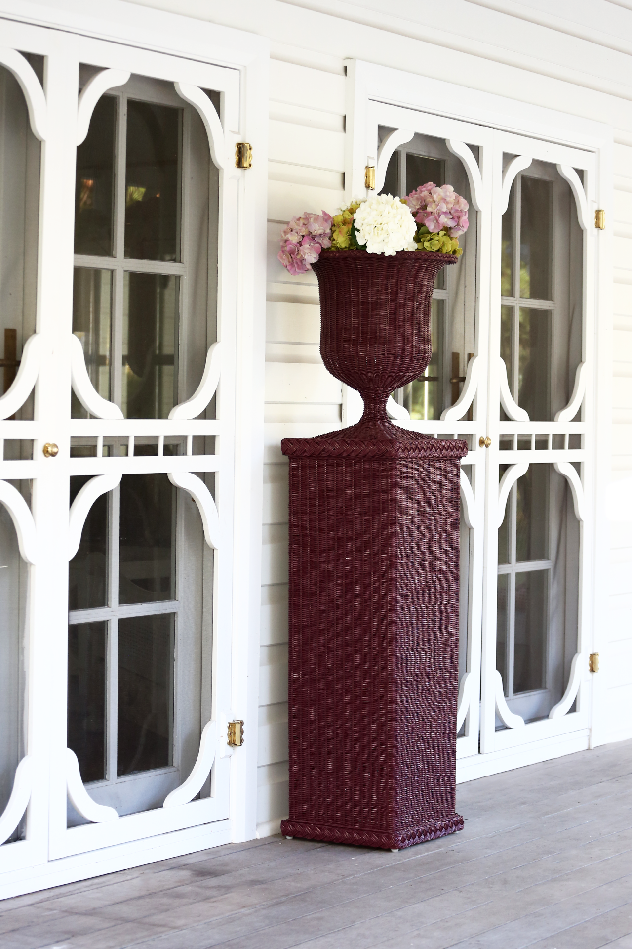 Handcrafted rattan urn-style vase with flowers, displayed on verandah