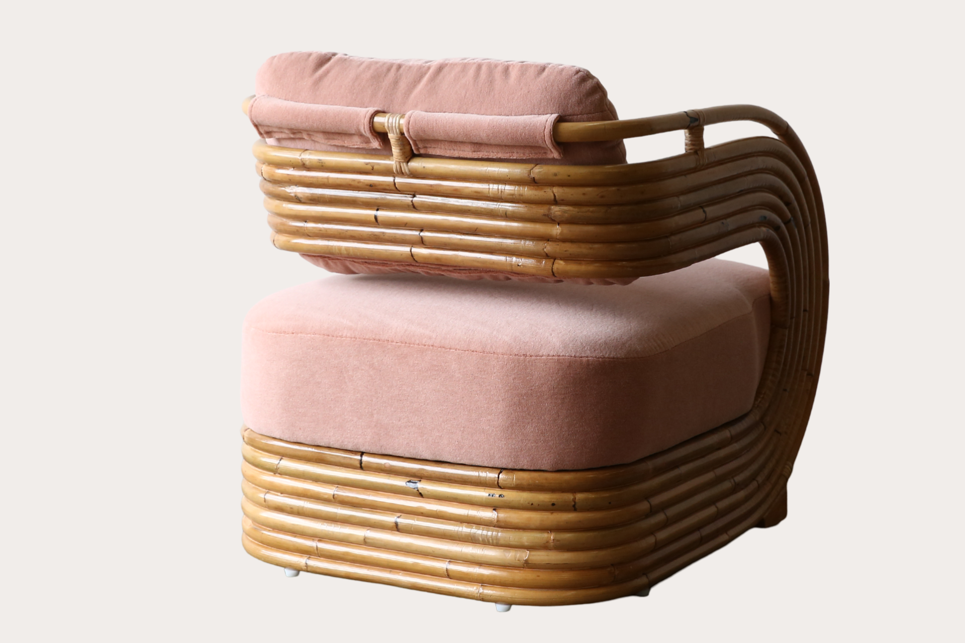 Rattan armchair with upholstered cushions in a pink velvet fabric.
