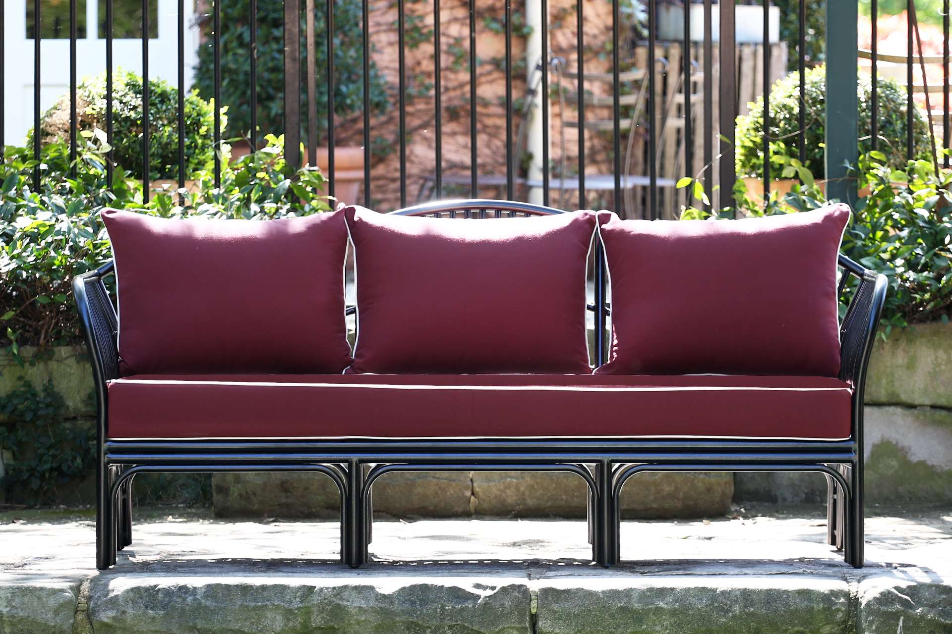 Black outdoor daybed with curved rattan frame and white cushions in a Mediterranean garden setting