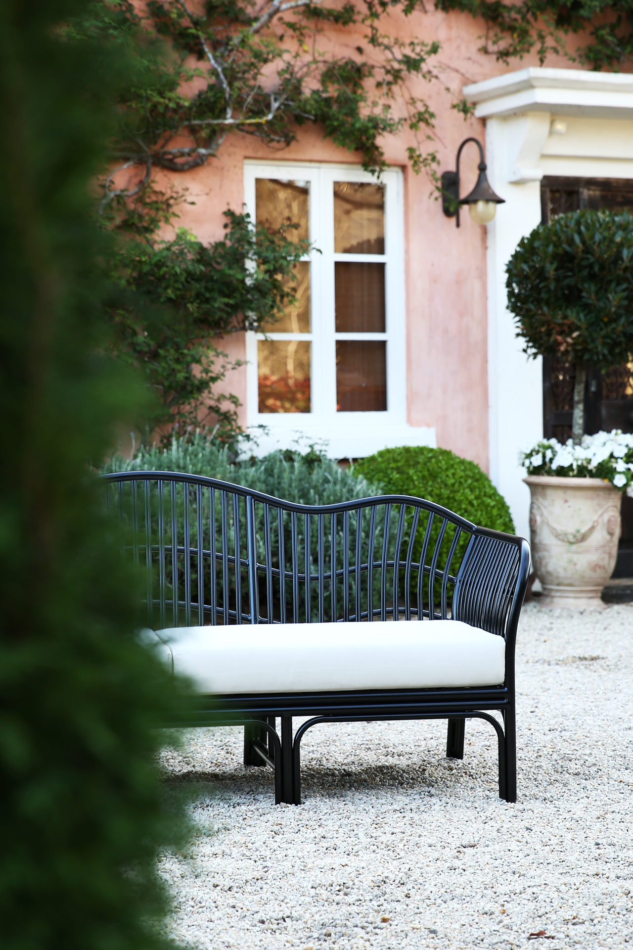 Black outdoor daybed with curved rattan frame and white cushions in a Mediterranean garden setting