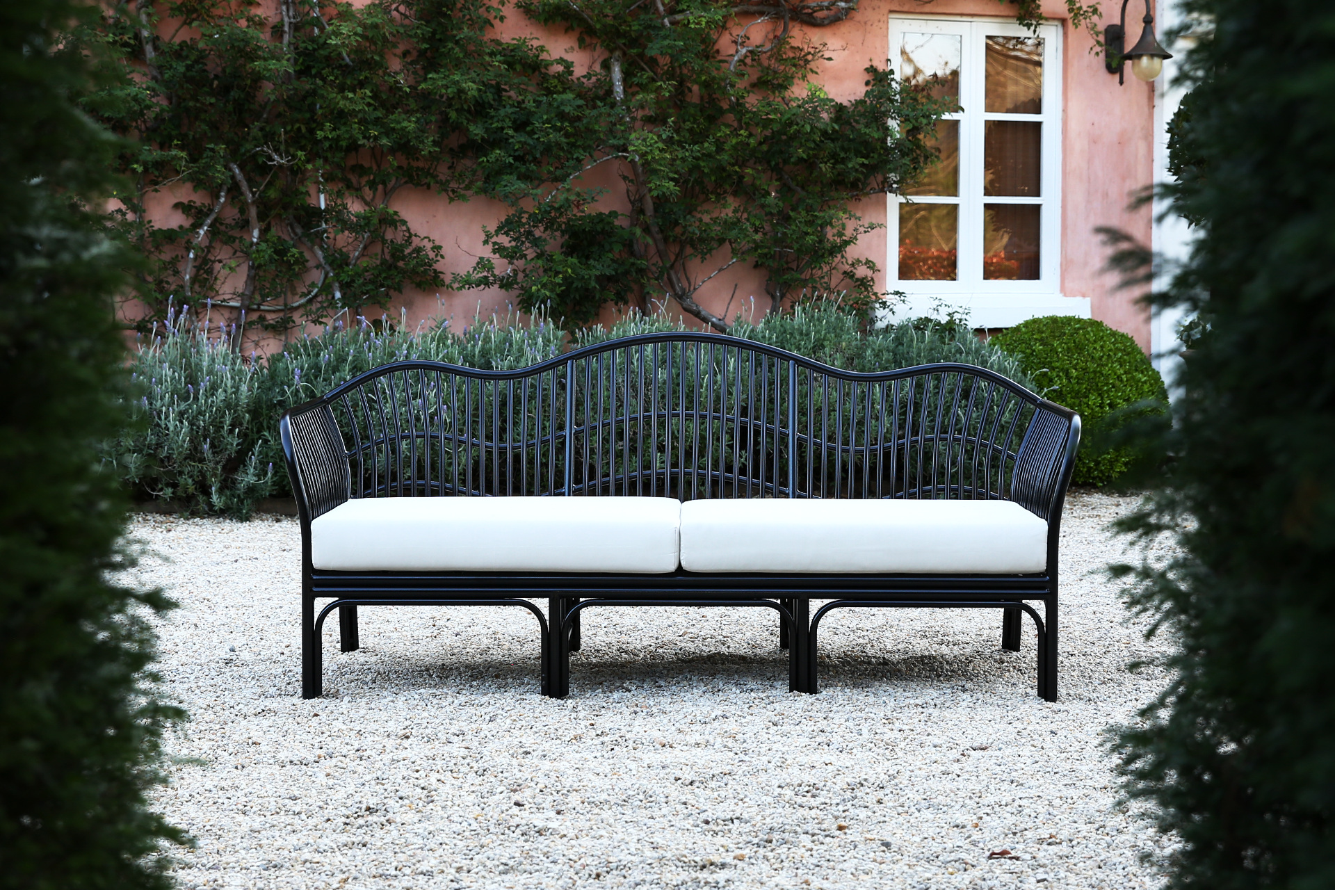 Black outdoor daybed with curved rattan frame and white cushions in a Mediterranean garden setting