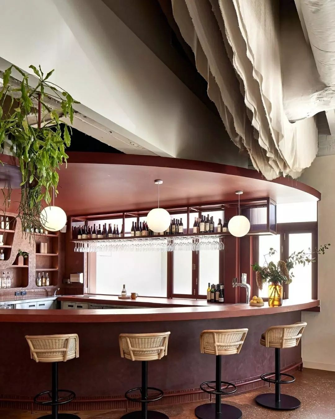 Rattan swivel bar stools at a curved hospitality counter with minimalist lighting and bottle display