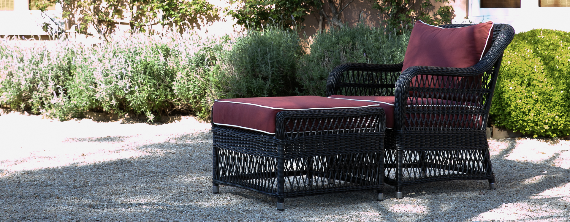 woven black outdoor wicker aluminium armchair with matching ottoman with cushions.