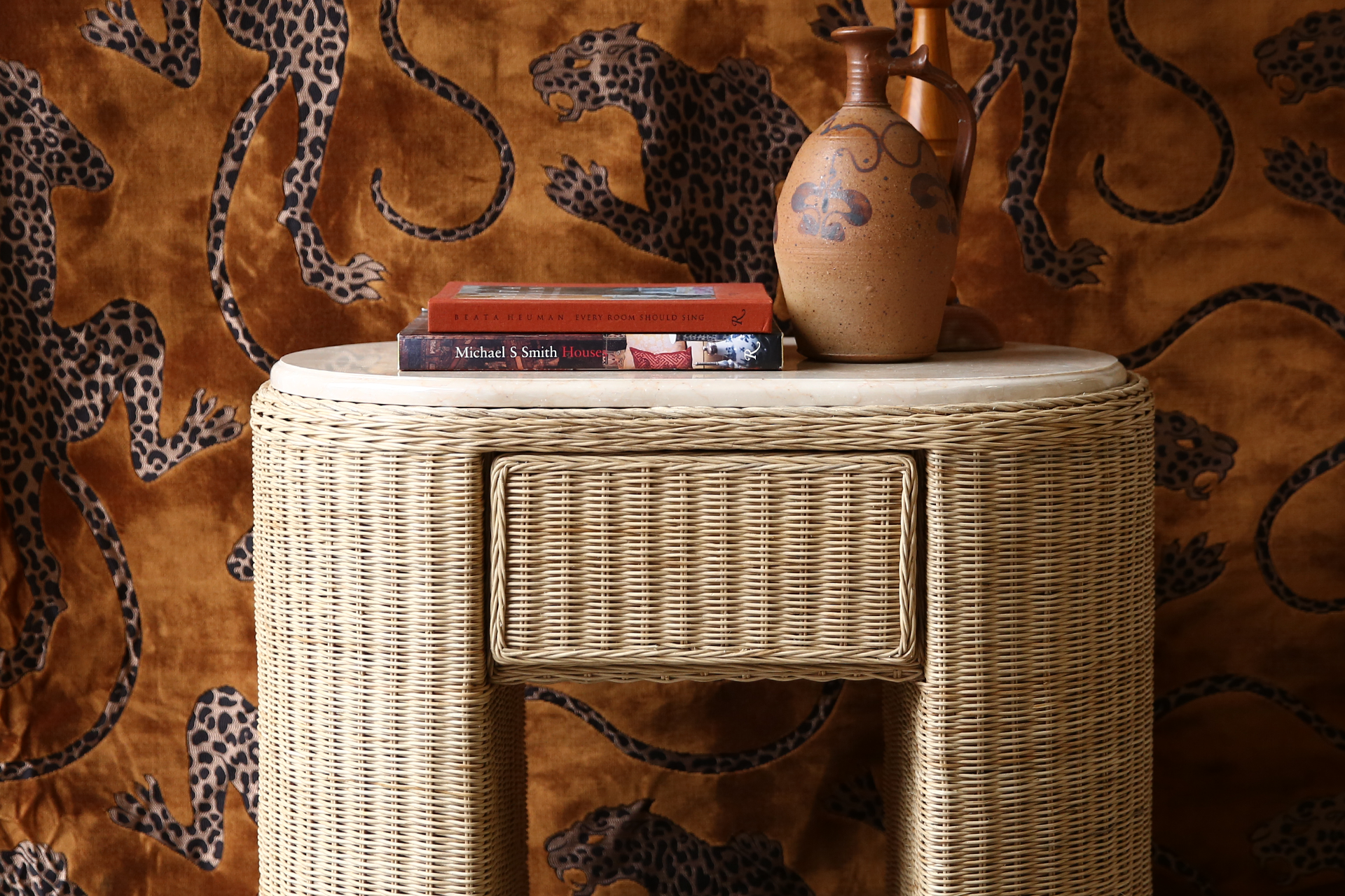 Wicker side table with books and a vase against a patterned wall.