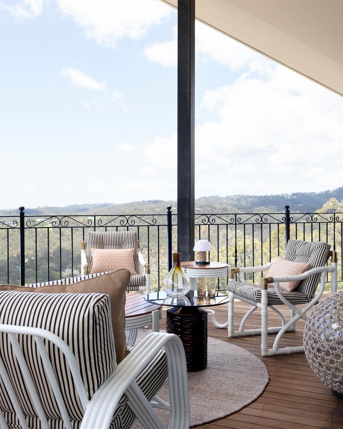 Outdoor balcony with white rattan lounge chairs, striped cushions, and scenic mountain views