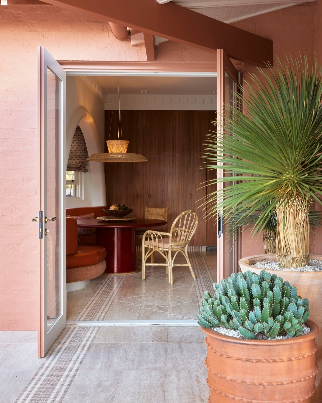 Rattan dining chair and curved banquette around a red lacquered table in a warm-toned Mediterranean interior